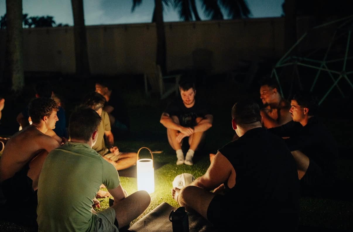 A small circle of people talking by lantern light