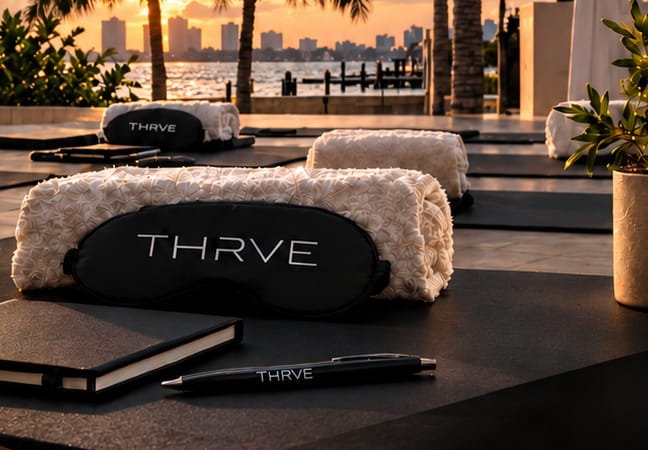 A THRVE towel, eye mask, booklet and pen laid out on yoga mats at sunrise