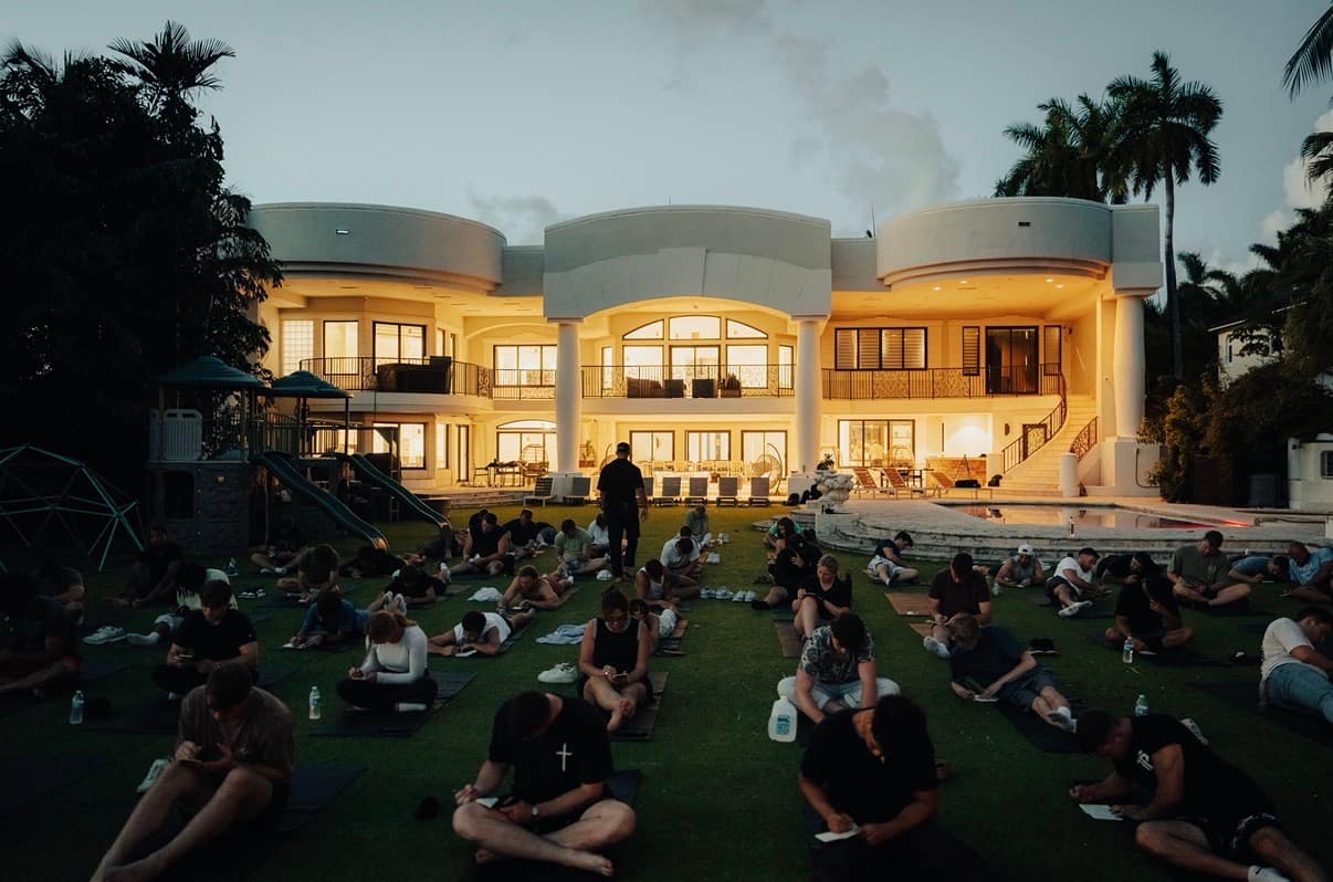 Guests lying on mats on a lawn at dusk during guided breathwork